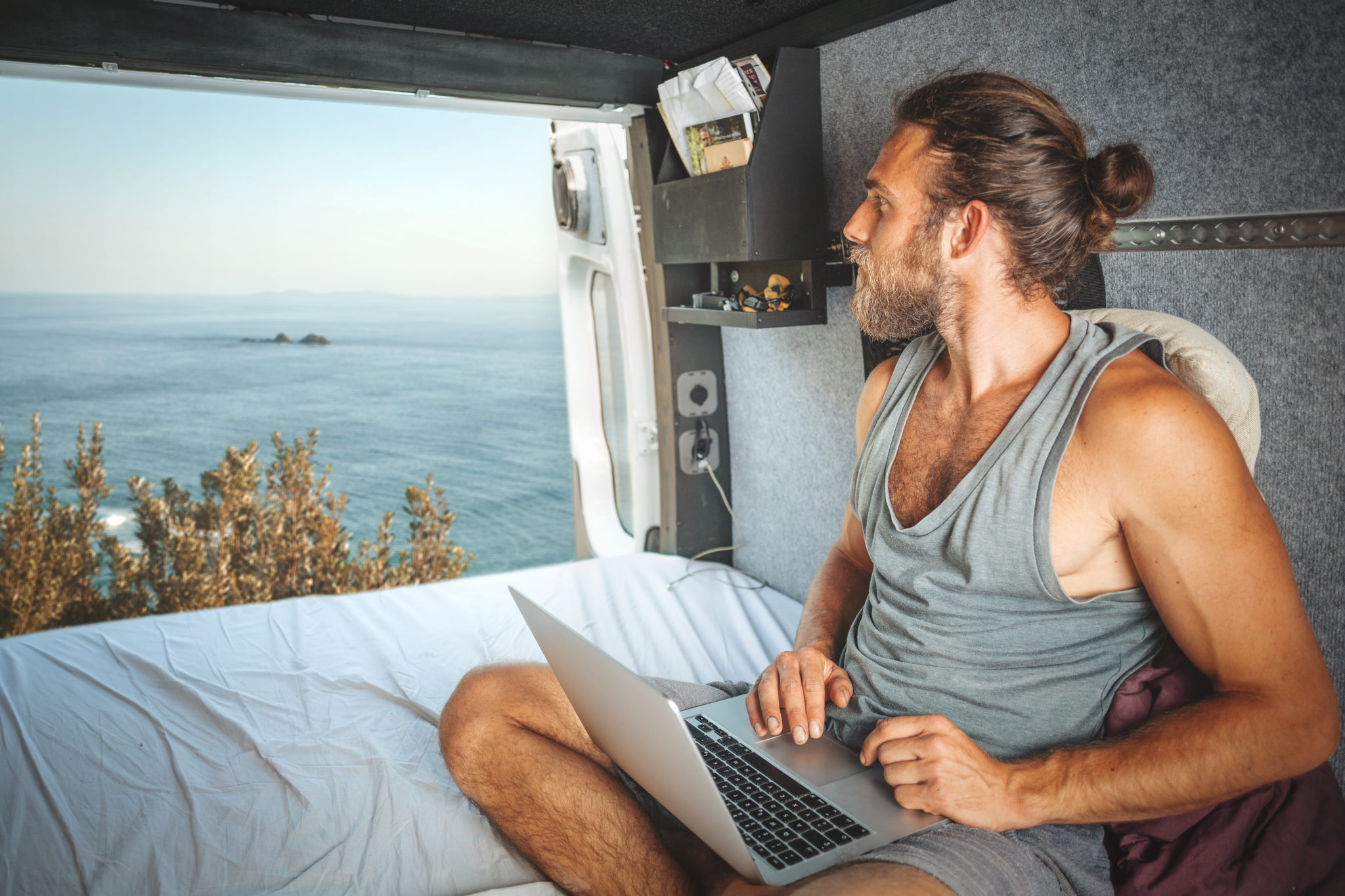 Man with a laptop inside his camper van is looking at the sea