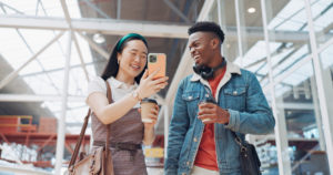 Shopping mall, smartphone and couple of friends on social media, website or blog for discount, sales and travel communication. Diversity gen z people walking, using phone or cellphone and coffee cup.